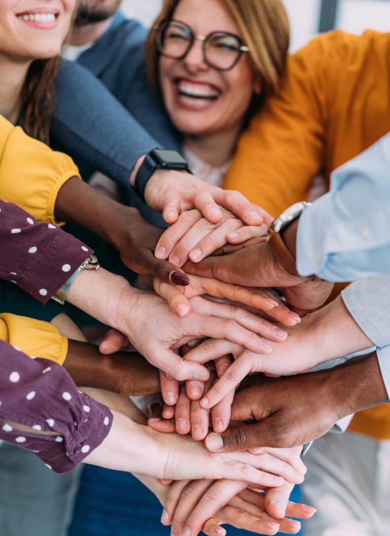 A diverse, happy, cohesive team with all hands in the center of a team huddle