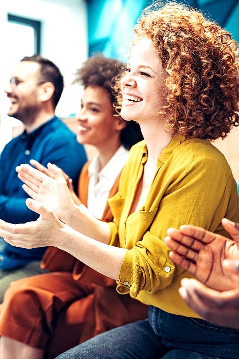 A woman with short curly red hair sitting among team members and clapping