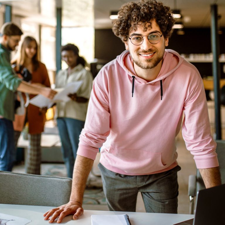 Confident, productive man at work with curly brown hair, wearing a pink hoodie
