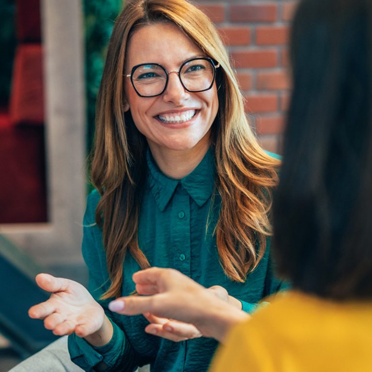 Two engaged and motivated employees talking enthusiastically about work. One woman is a redhead, the other is a brunette