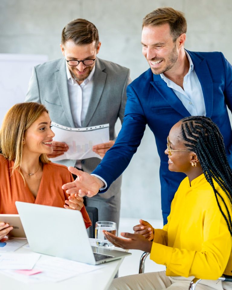 team-collaboration-img A team collaborating at work and talking about a project being showcased on a laptop
