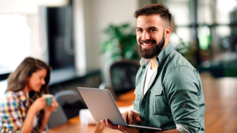 Intrinsically motivated person sitting on a desk with a computer, coworker in the background.