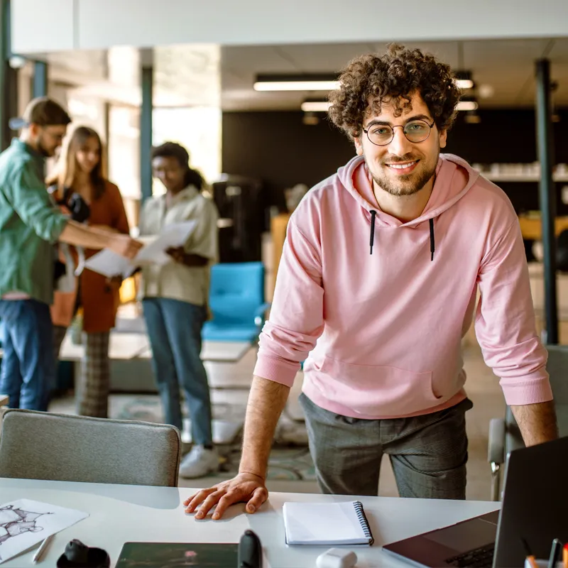 Man at work smiling with coworkers in the background.