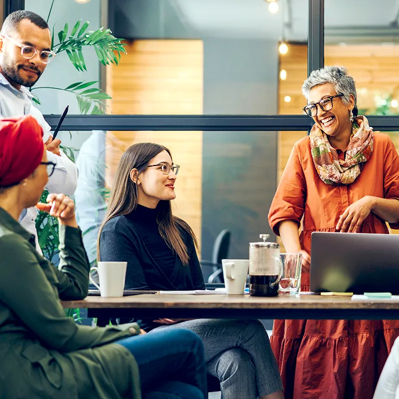 A woman telling a funny story to her coworkers while drinking coffee together.
